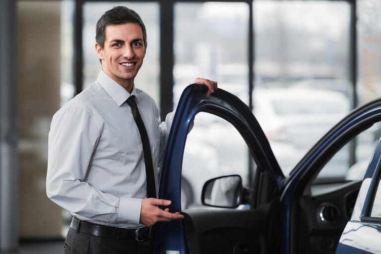A person discusses paperwork and pricing details with a sales consultant at a dealership desk.