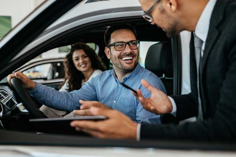 A couple reviews a vehicle contract with a sales representative in a dealership office.
